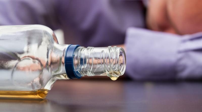 Drunk man sleeping with almost empty bottle of alcohol