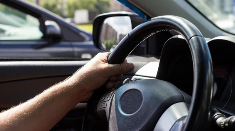 Man's hands holding steering wheel while driving car on city road.